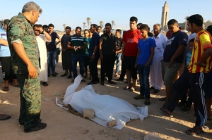 Lidé stojí u jedné z dvanácti mrtvol ilegálních imigrantů ležící na pláži u Tripolisu.